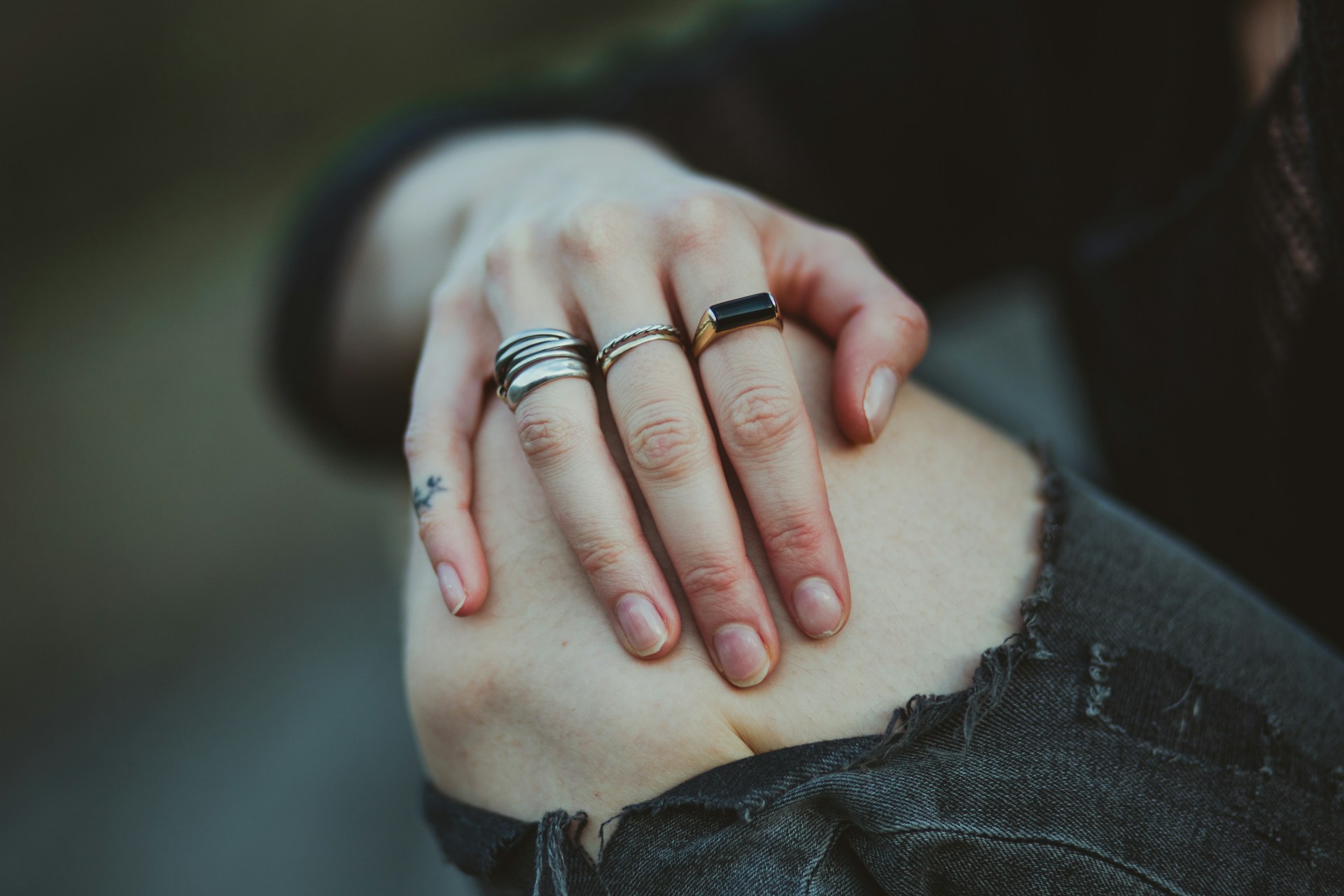 a person has one hand resting on their bare knee, seen through their torn black jeans