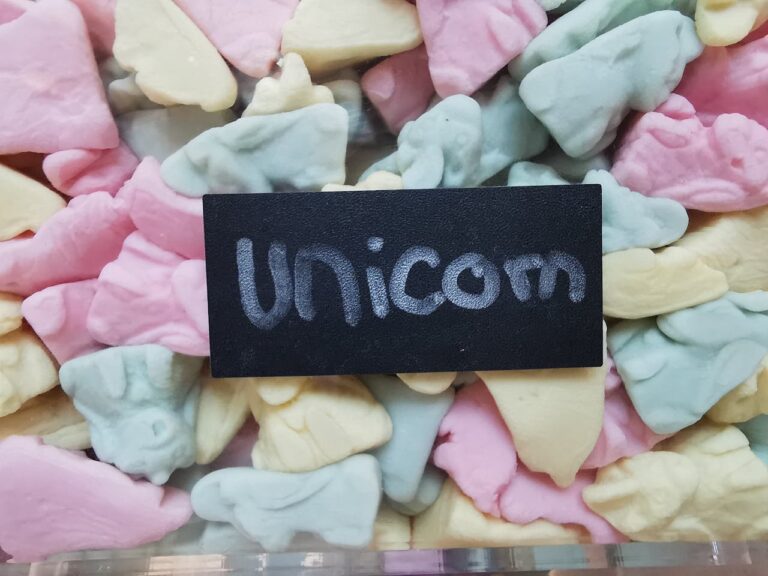 A vibrant assortment of unicorn-shaped pastel candies with a black sign resting on top that says unicorn