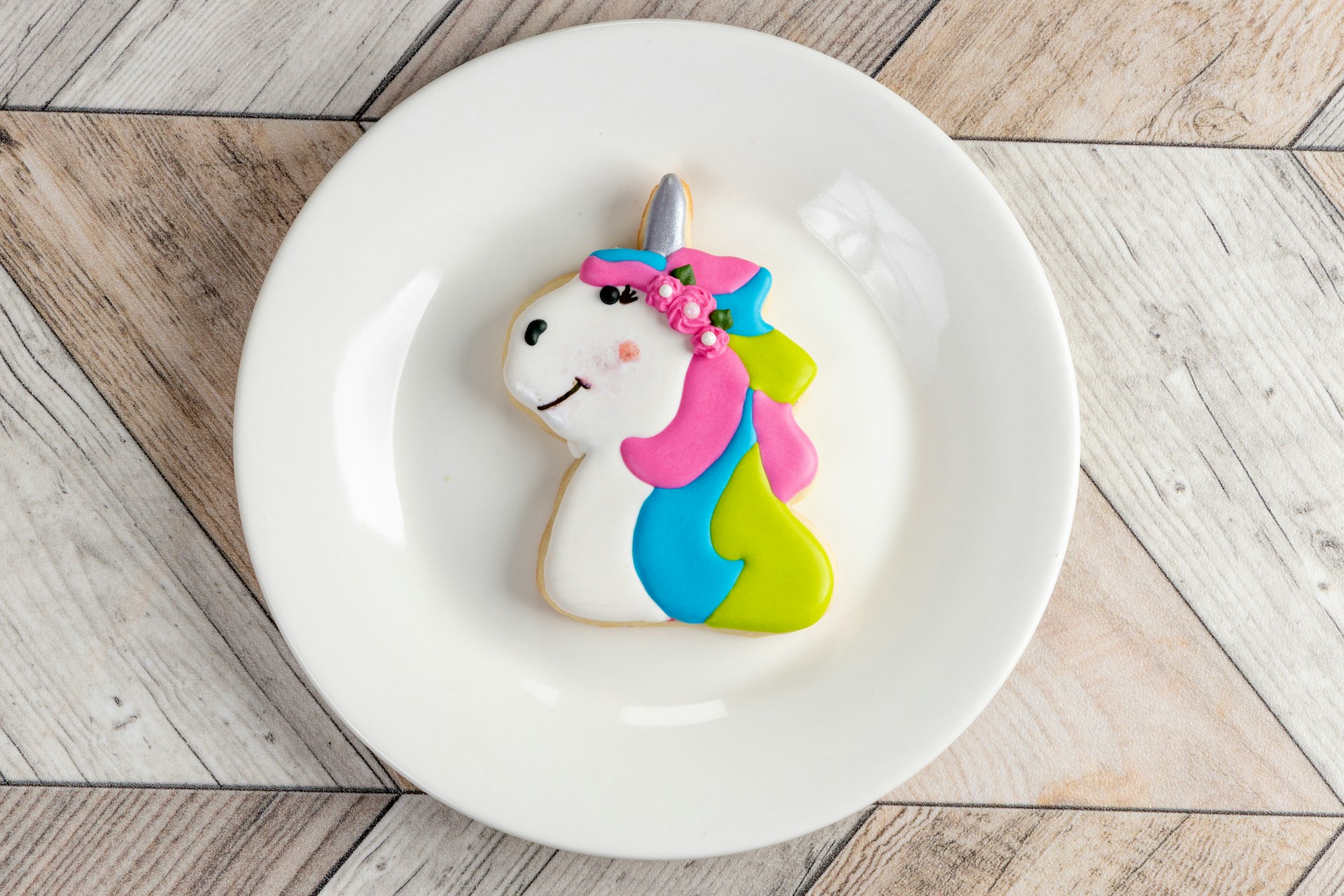 A unicorn cookies with a pink, green, and blue mane sits in the middle of a white plate