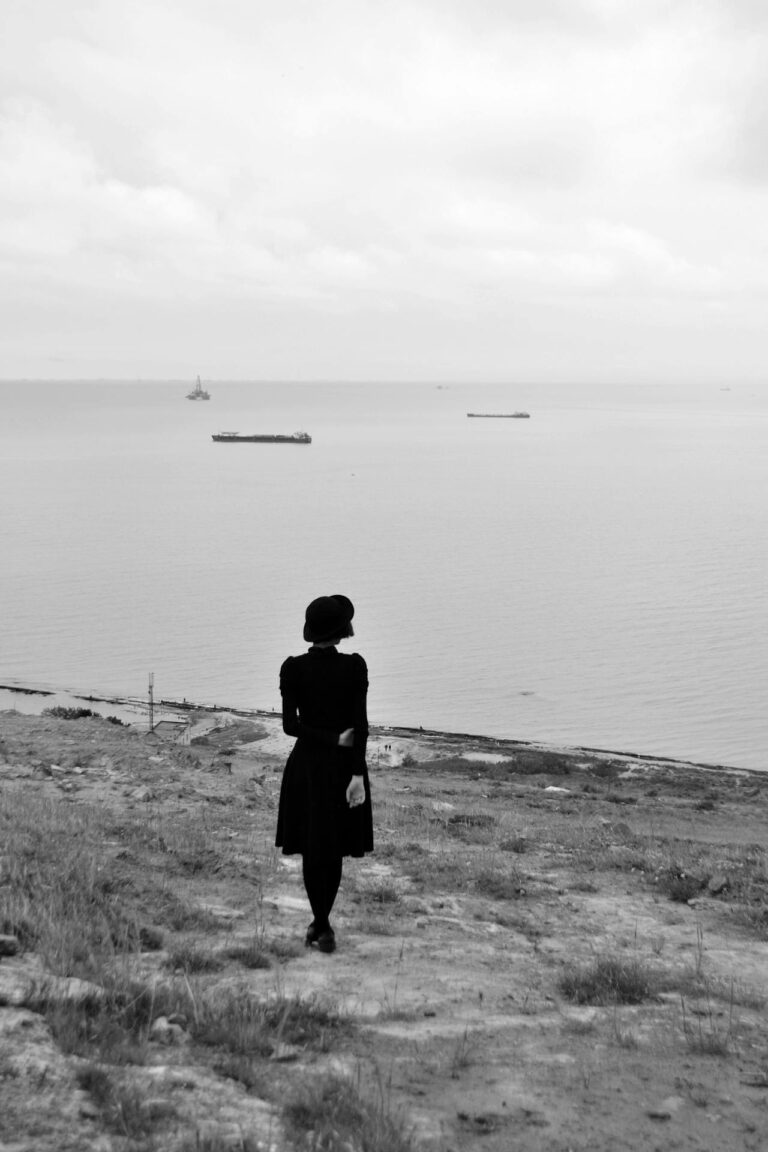 Silhouette of a woman standing calmly on a cliffside, overlooking the serene sea.