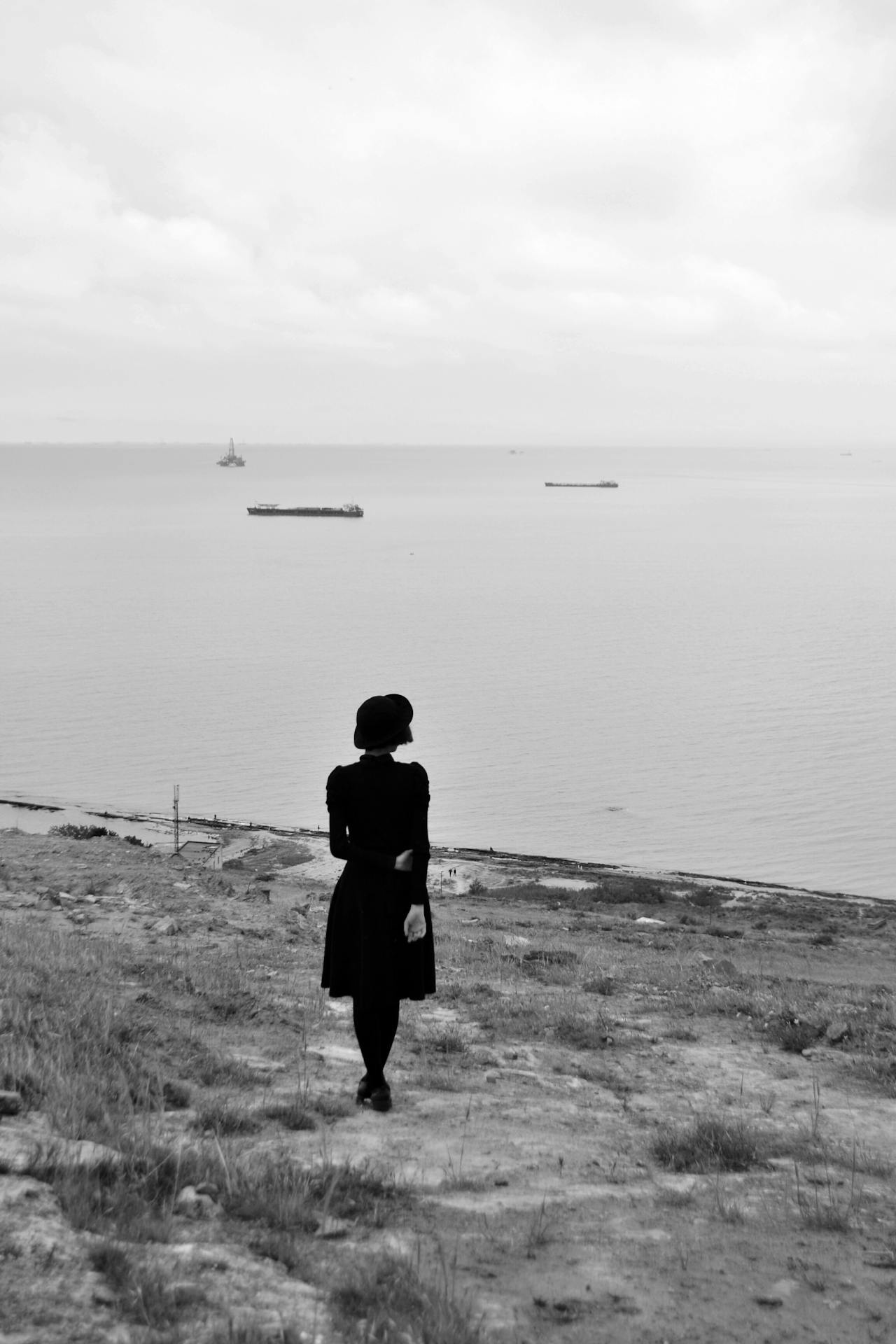 Silhouette of a woman standing calmly on a cliffside, overlooking the serene sea.